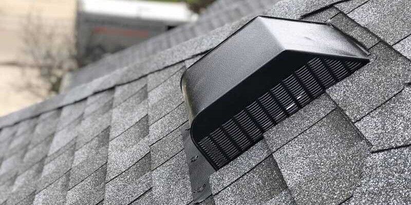 A black box roof vent installed on a roof with gray shingles.