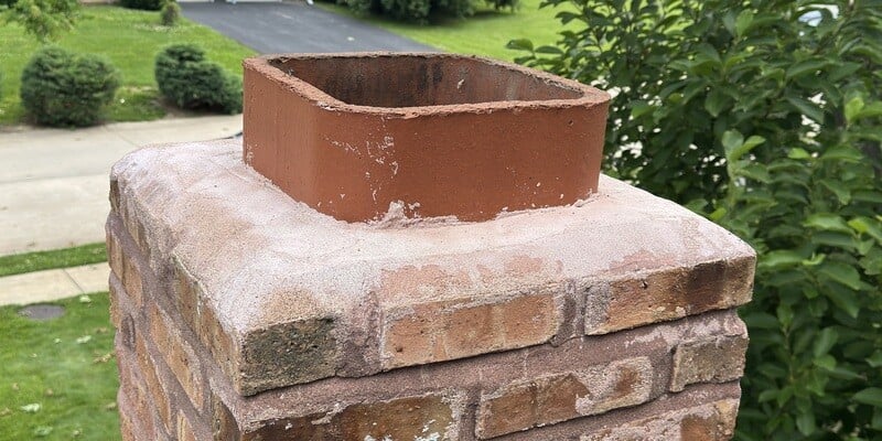 An image of a square clay flue tile protruding a few inches from a masonry chimney flue.