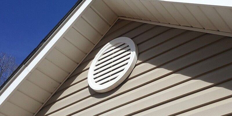 The facade of a home with a white, round gable end vent installed over the beige siding.