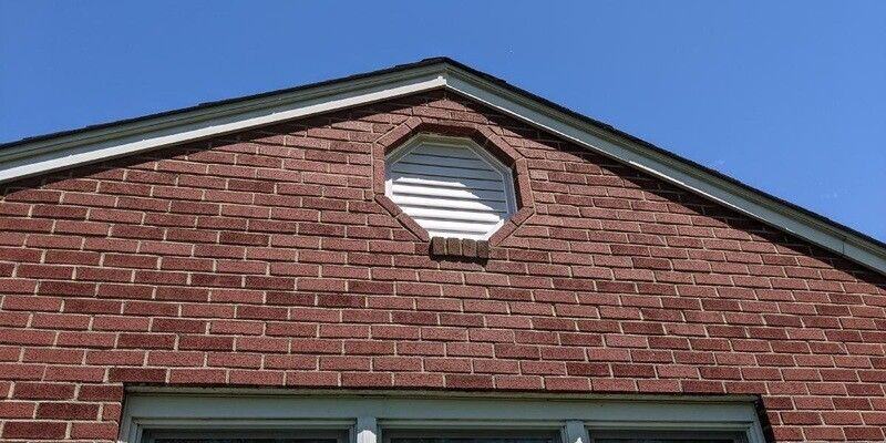 A white, octagonal gable end vent installed on the side of a house with a brick face.