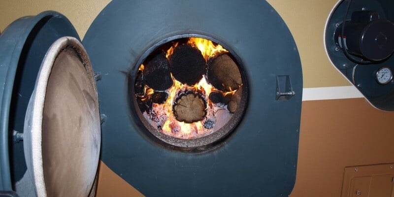 A close-up of the open door of a GARN wood boiler. A pile of firewood can be seen burning up within the unit.