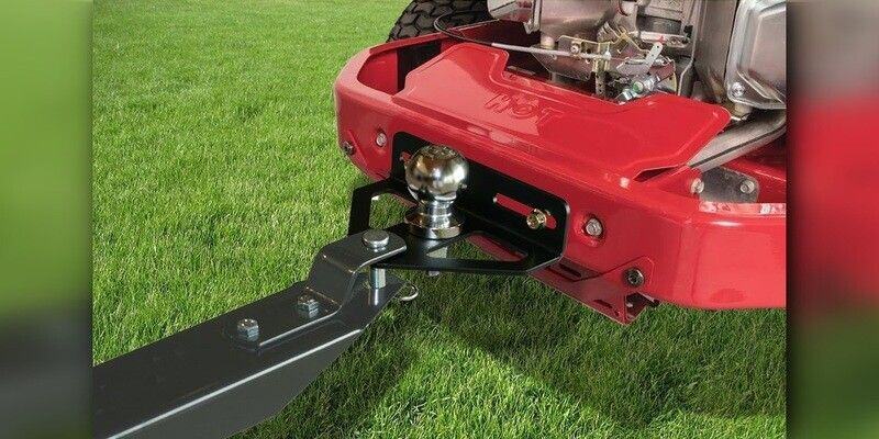 A Good Vibrations Z-Hitch Zero-Turn Hitch Plate attached to a red zero-turn mower. Grass can be seen underneath.