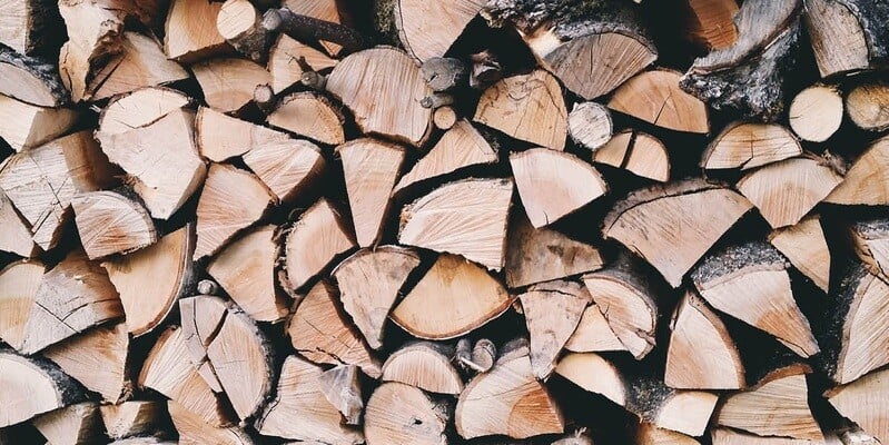 A closeup of a stack of split cordwood. The logs are split into fourths, and there are a few dozen of them in the shot.