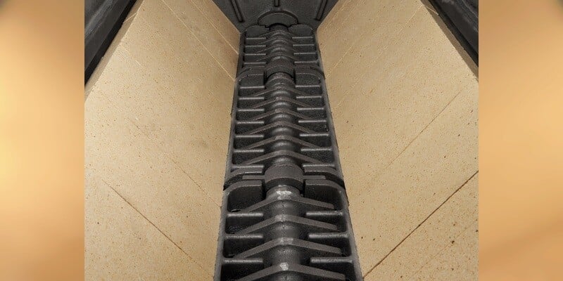 A close-up of the inside of an Ignite Tech HD80 Indoor Wood Furnace's firebox. Visible is the firebrick and the furnace's cast iron roller grate.