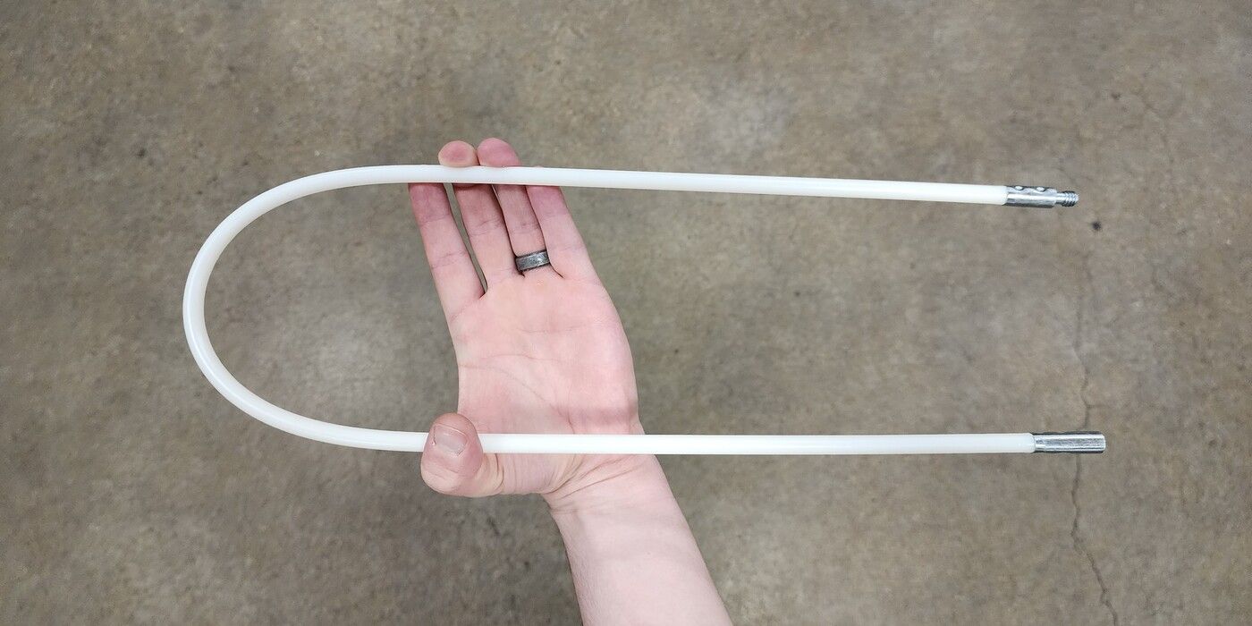 A hand holding a LintEater connector rod. The rod is bent 180 degrees. There is a concrete floor in the background.