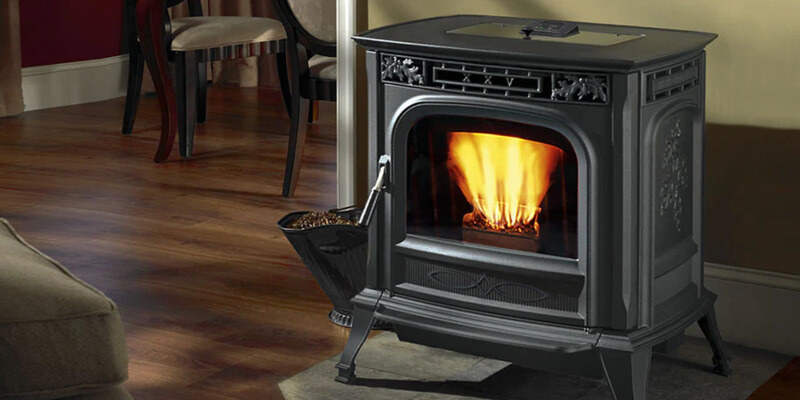 A wood pellet stove situated in a living room. The stove has a bucket of pellets sitting just to its right. A fire roars in its firebox.