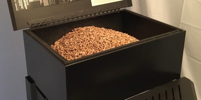 A pellet stove with its top hopper open. Several pounds of wood pellet fuel have been poured into the hopper.