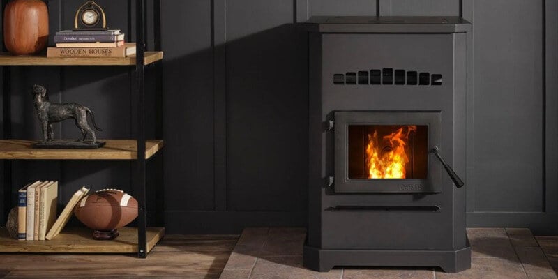 A wood pellet stove installed in a sleek, modern-looking room. The wall behind it is black. A shelf full of tchotchkes sits to the left of the stove.