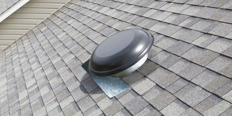 A gray powered roof vent installed on a roof with gray shingles.