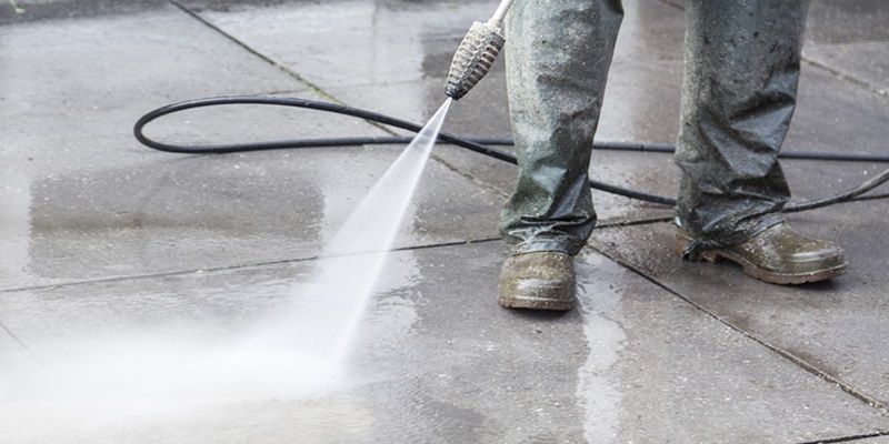 A person with heavy-duty rubber boots on cleaning a concrete surface with a pressure washer.