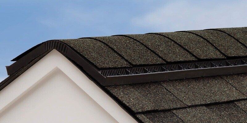 A roof ridge vent installed on a roof with dark-gray shingles. The roof vent has hip and ridge shingles installed on top of it.