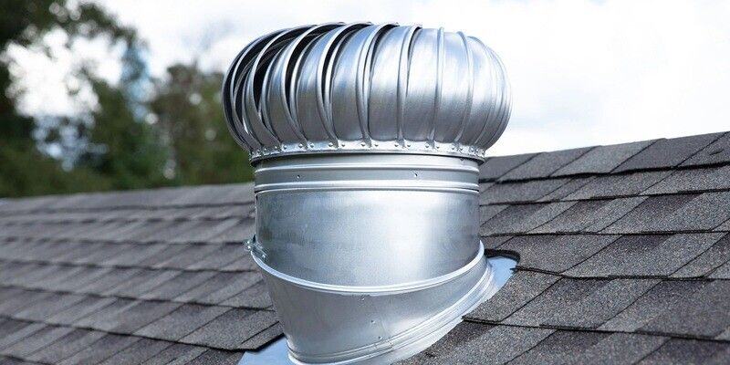 An unpainted metal roof turbine vent installed on a roof with gray shingles.