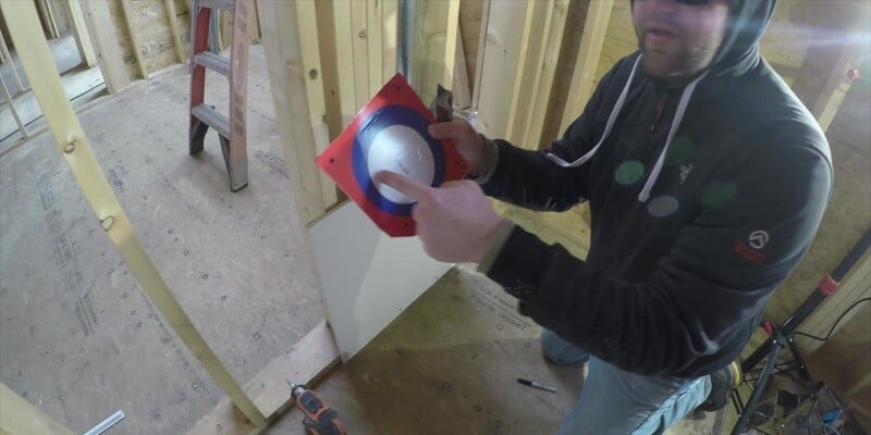 A man holding up the stencil of a SnugDryer dryer vent connector kit. He is pointing to the innermost white circle of the stencil.