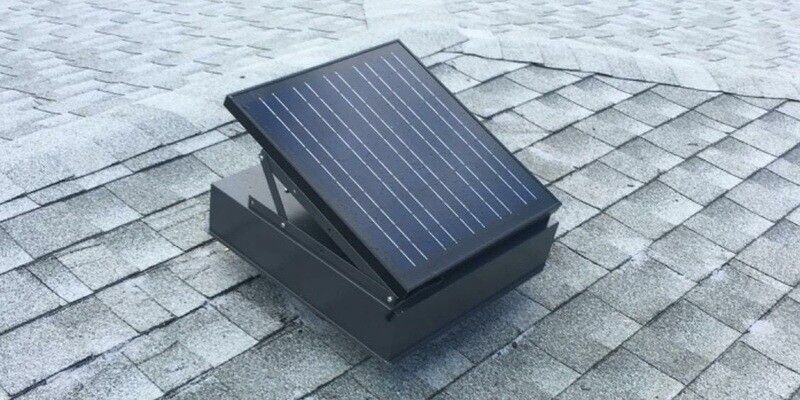 A solar-powered roof vent installed on a roof with light-gray shingles.