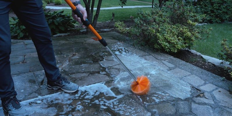 A man using a SpinAway rotary cleaning brush to clean a stone patio. The patio surface is covered in soapy water.