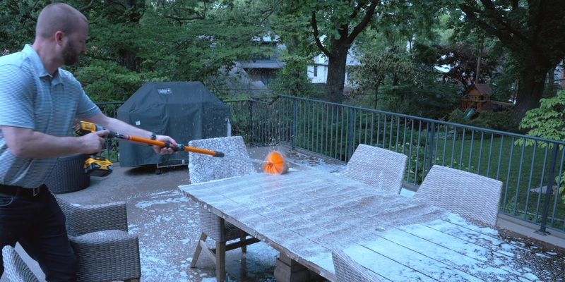 A man using a SpinAway rotary cleaning tool to clean a wooden table on a back patio. The table is covered in soapy water.