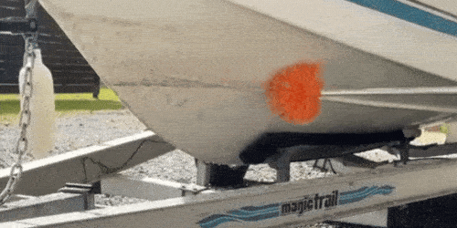 A GIF of a SpinAway rotary cleaning brush scrubbing black stains from the hull of a mid-sized fishing boat.