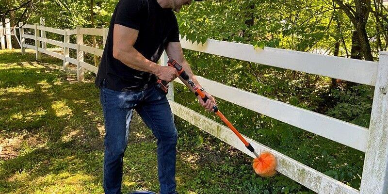 A man using a SpinAway rotary cleaning brush to clean grass stains off of a white vinyl fence.
