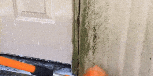 A GIF of a SpinAway rotary cleaning brush being used to clean grass stains off of corrugated metal siding.