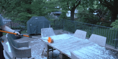A GIF of a man using a SpinAway rotary cleaning brush to clean off a wooden patio table. The patio table is covered in soapy water.