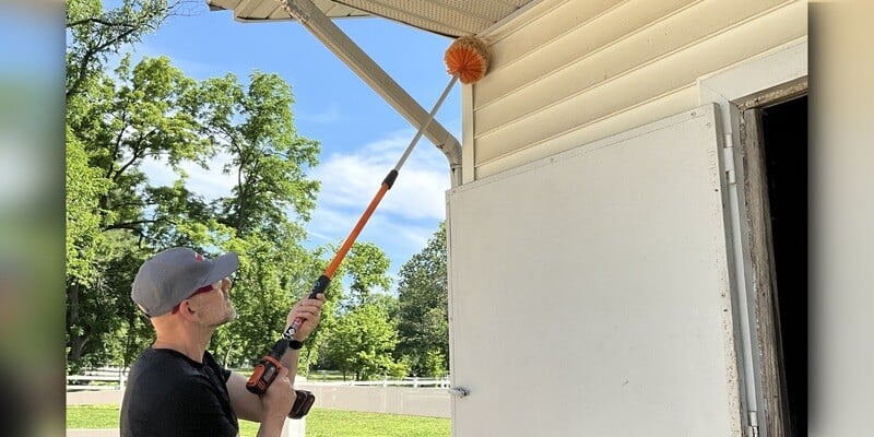 A man using a SpinAway rotary cleaning brush to clean the eave next to the downspout of a house.