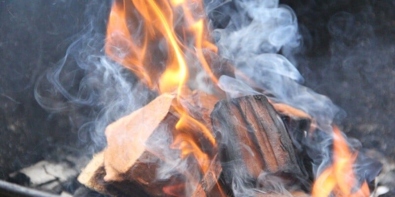 A closeup of a pile of campfire wood. The wood is just minutes into burning, so it's hardly charred. It's producing a lot of smoke.