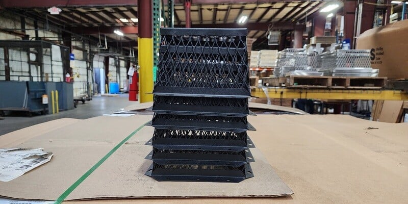 A stack of six black HY-GUARD EXCLUSION Universal VentGuards on top of a pile of cardboard. The HY-C factory is visible in the background.