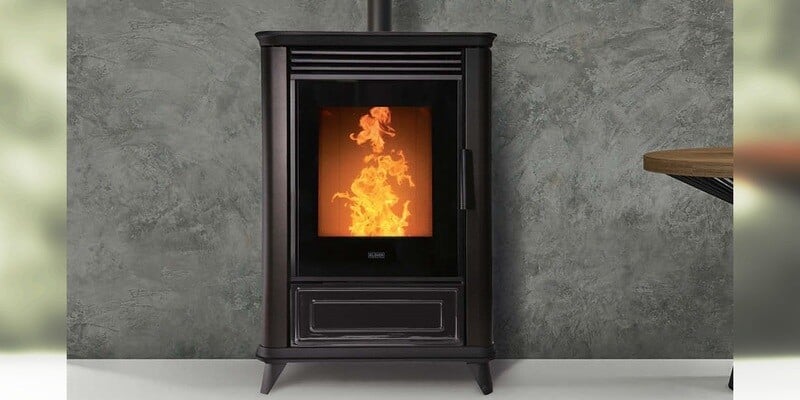 A wide-angle shot of a wood pellet stove installed in a very modern-looking room. The stove rests against a concrete wall.