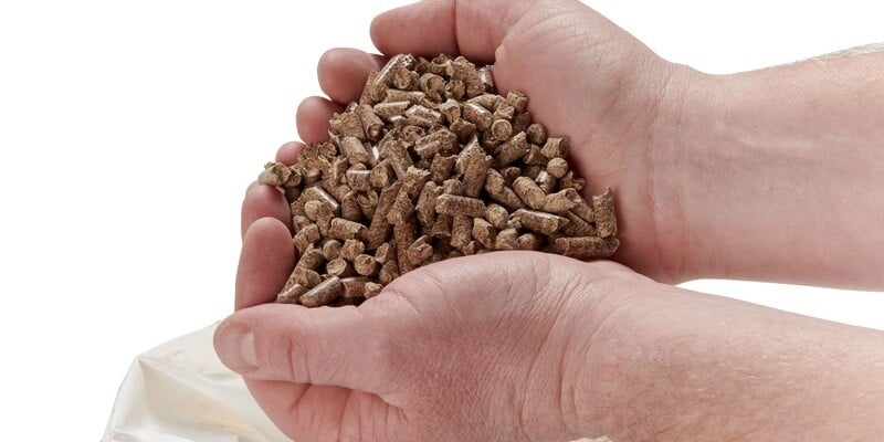 A pair of hands holding a handful of wood pellet fuel against a white background.