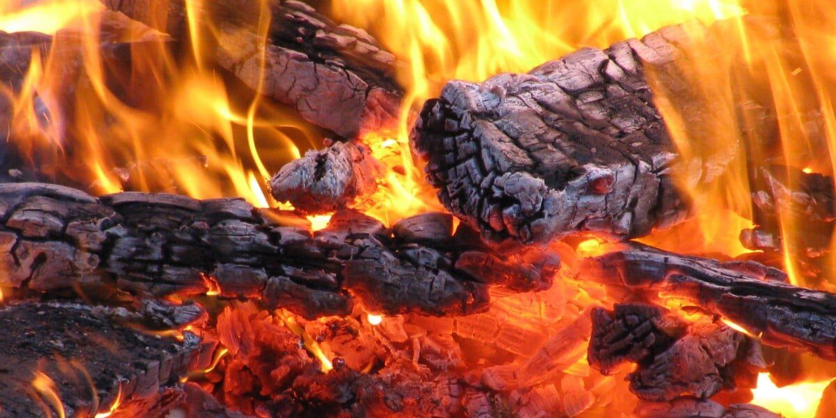 A close-up of logs that are nearly burnt to ash. They are engulfed in flames.