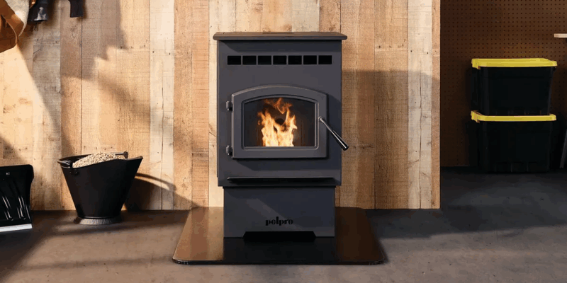 A PelPro pellet stove installed in a garage. The unit sits atop a stove board against a wood panel wall. A bucket of pellets sits by the unit.