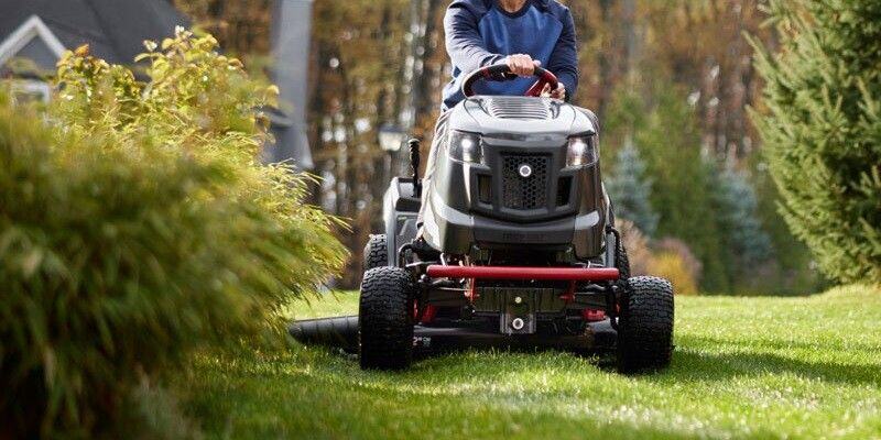 A man using a Troy-Bilt riding lawn mower to cut his grass.