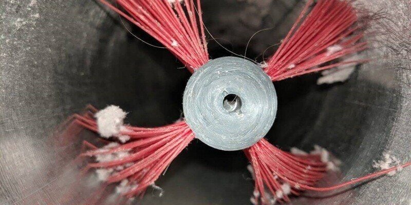 A closeup of a dryer vent cleaning kit head inside of a dryer vent. The bristles of the kit's head have a bit of lint collected around them.