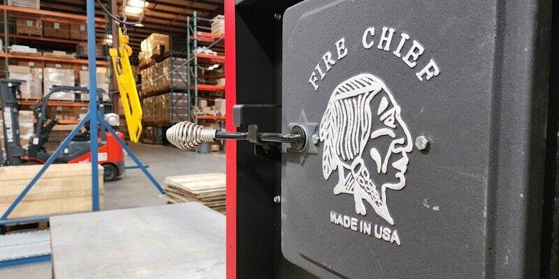 A close-up shot of the front door of a Fire Chief FC1000E Wood Burning Furnace. In the background, the factory in which it was built is visible.