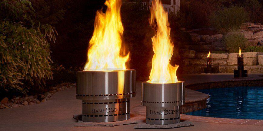 Two Flame Genie fire pits on a back patio by a pool at night. Both fire pits have a fire going in them.