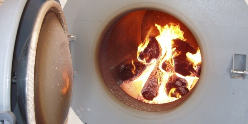 A closeup of a GARN GN2000 wood boiler. Its combustion door is open, and a fire is burning fully inside the unit.