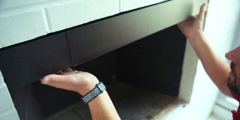 A man pushing a Liberty Foundry Co. Smoke Guard against the top of his fireplace to its installation location.