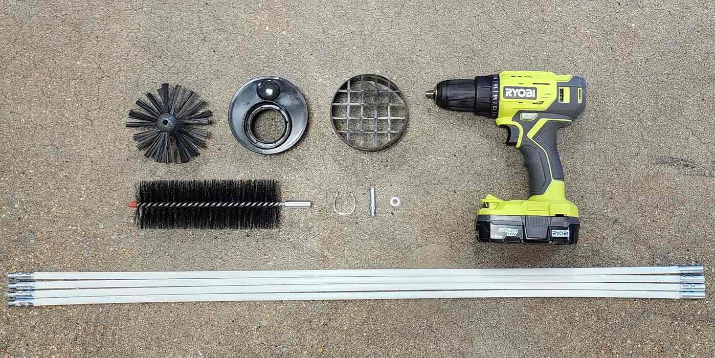 The contents of a LintEater dryer vent cleaning kit laid out on a concrete floor next to a RYOBI drill.