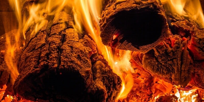  A closeup of cordwood burning inside of a wood furnace. Fresher, newer wood sits atop a bed of burning coals.