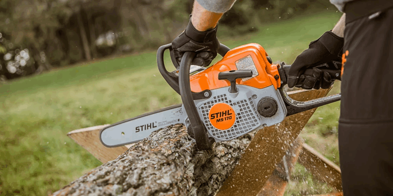 A man using a gas-powered STIHL chainsaw to cut through a log in his yard.